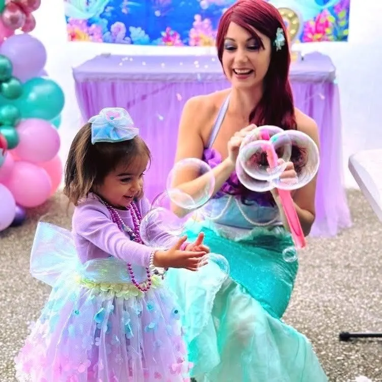 Little Mermaid Ariel party entertainer blowing giant bubbles for a clapping toddler in pastel mermaid dress at a Melbourne under-the-sea birthday party