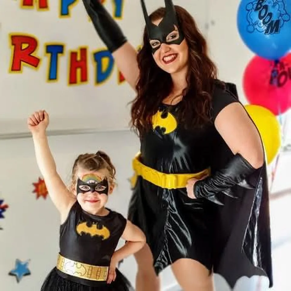 Batgirl superhero party entertainer in black cape and yellow bat logo posing with young girl in matching Batgirl costume and mask at a Melbourne superhero birthday party