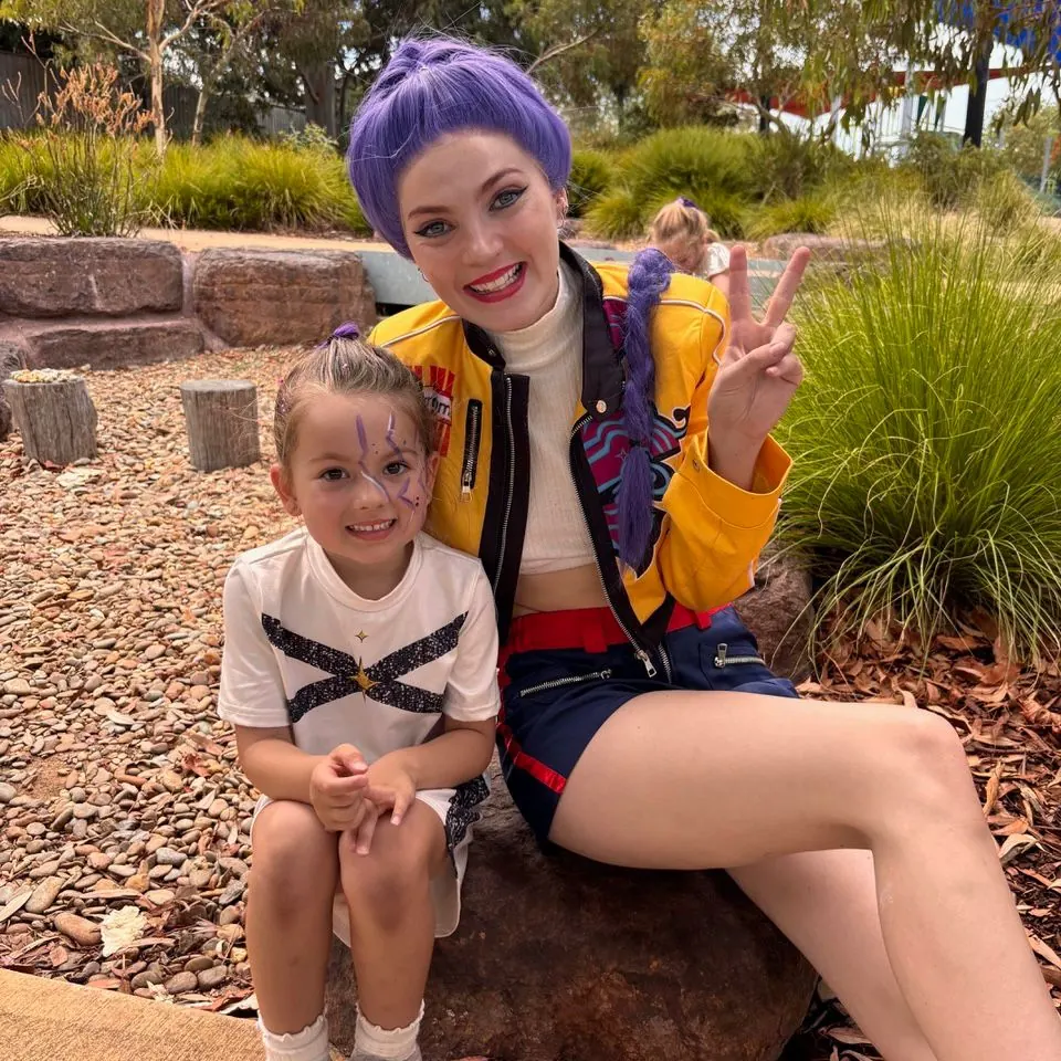 Zombies themed kids party with Dreamscape entertainer in purple hair and yellow jacket posing with young birthday girl outdoors in Melbourne