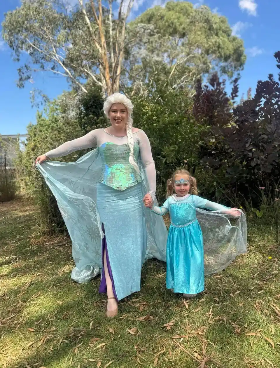 Frozen Elsa party entertainer in sparkling blue gown holding hands with young girl in Elsa dress and tiara in a sunny Melbourne garden princess party