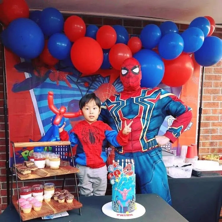 Iron Spider entertainer posing with boy in Spider-Man costume in front of red and blue balloon arch and Spider-Man birthday cake in Melbourne