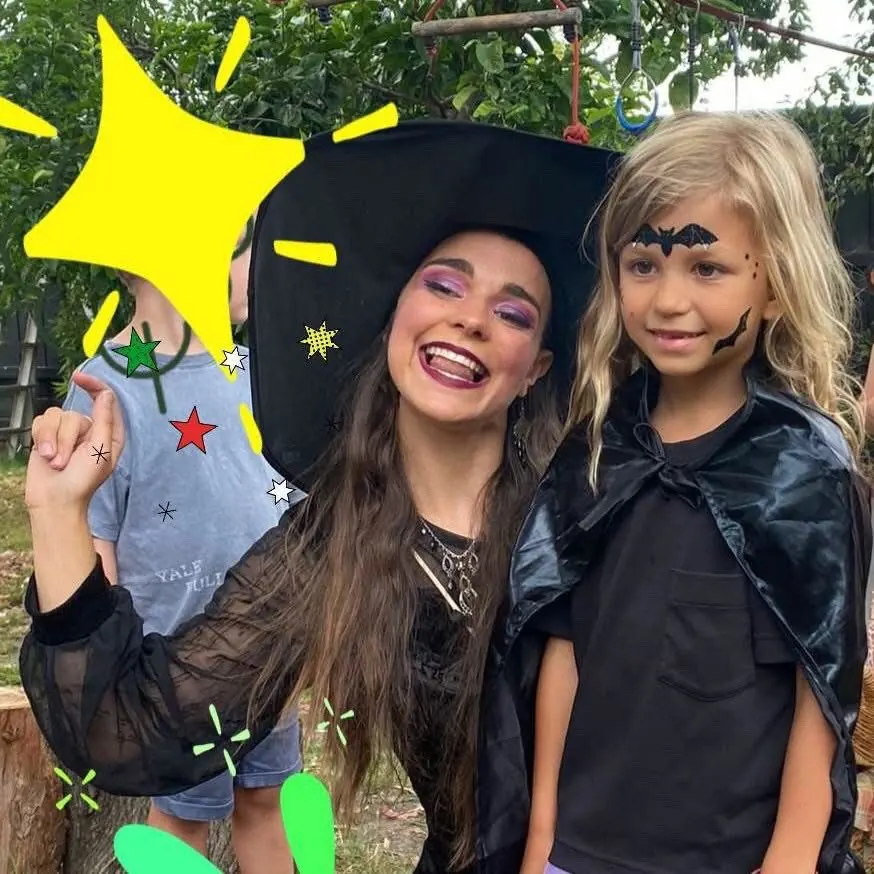 Witch party entertainer laughing with young girl wearing black bat face paint and cape at an outdoor Halloween kids party in Melbourne