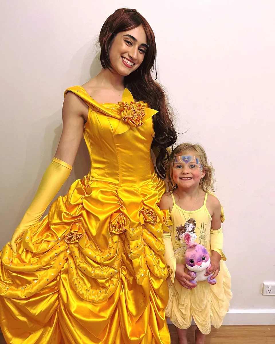 Princess Belle party entertainer in yellow Beauty and the Beast ballgown posing with smiling toddler in matching yellow Belle dress and princess face paint at a Melbourne princess birthday party