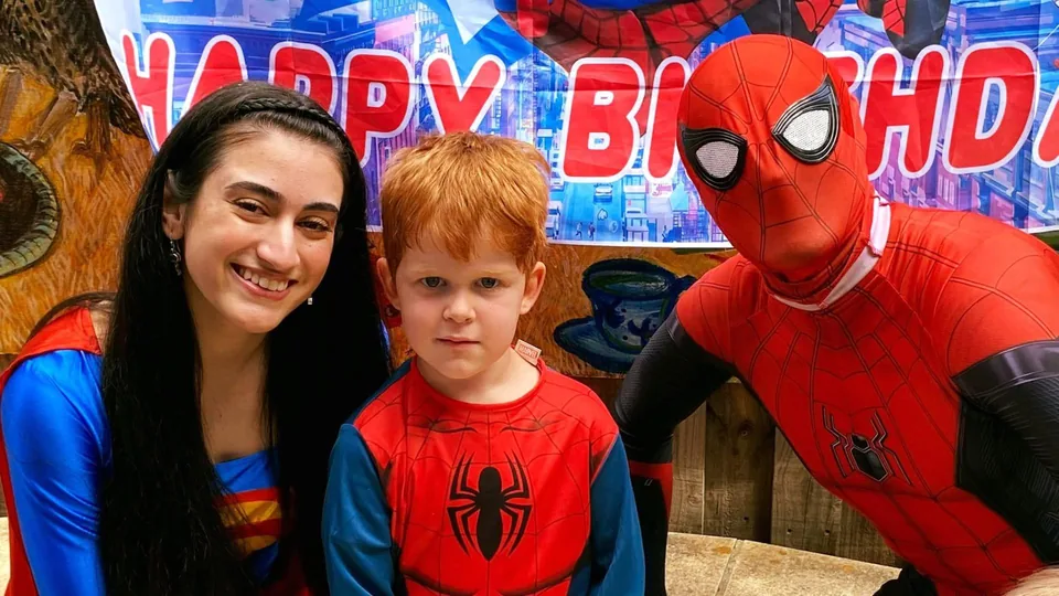 Superwoman and Spider-Man party entertainers posing with young boy in Spider-Man costume in front of Happy Birthday Spider-Man banner at a Melbourne superhero birthday party