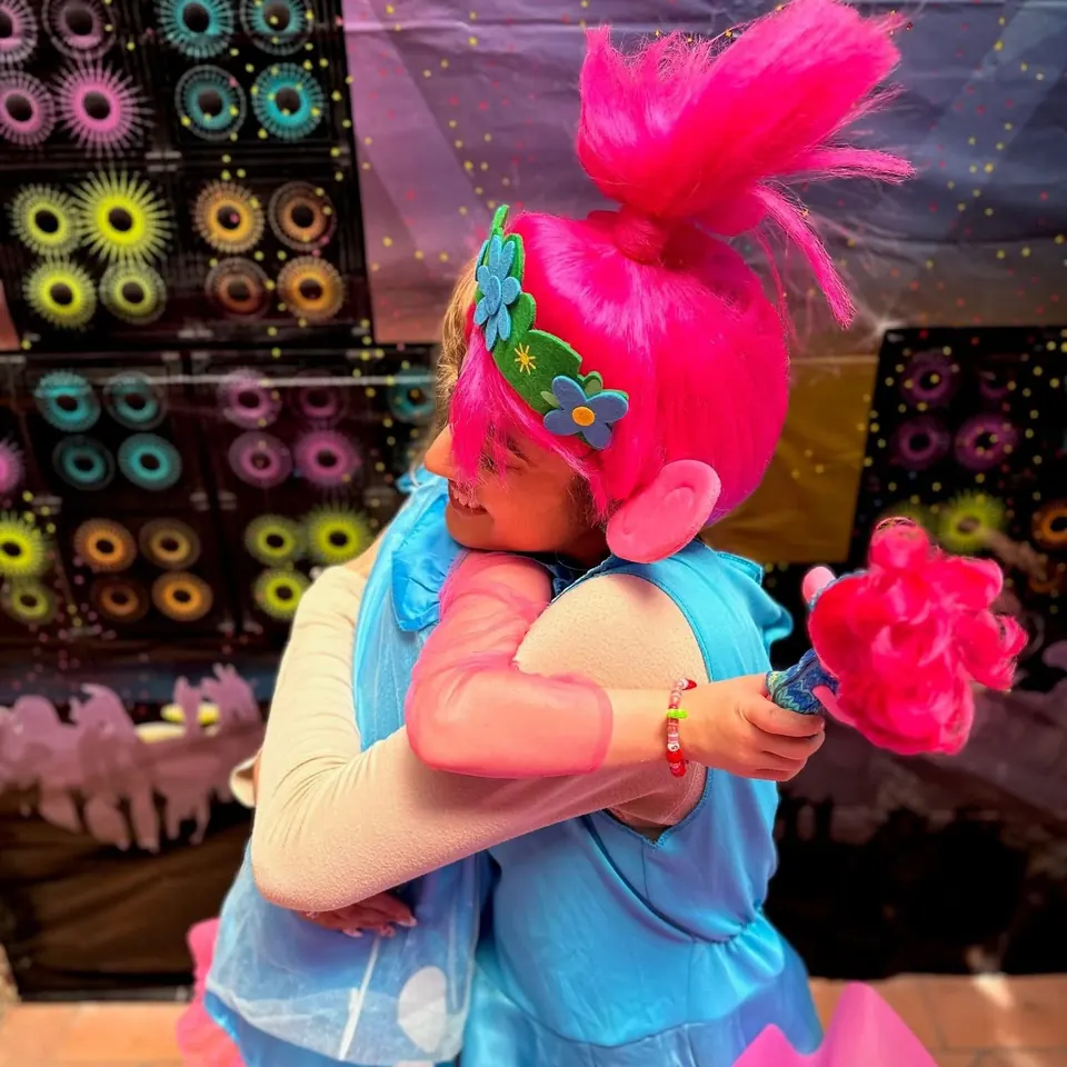 Trolls Princess Poppy party entertainer with hot pink hair and flower crown hugging young girl at a Melbourne Trolls themed kids birthday party