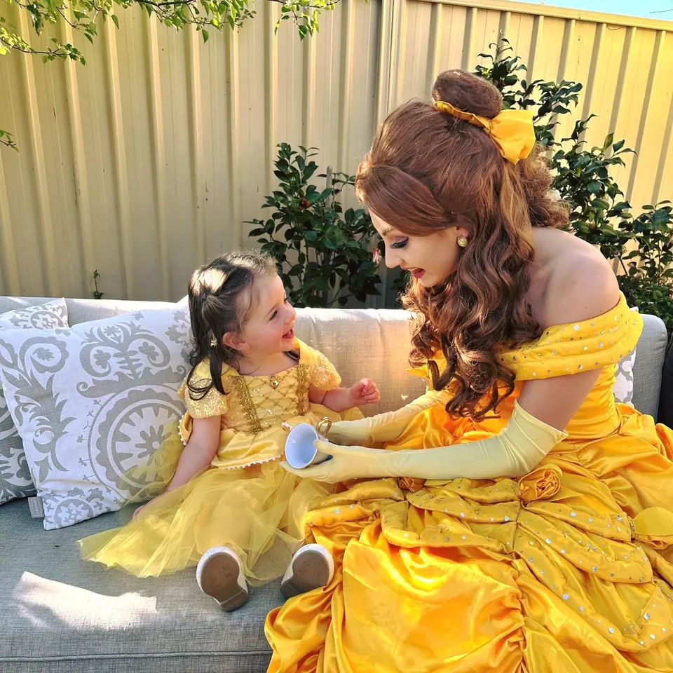 Princess Belle party entertainer in yellow Beauty and the Beast gown sharing a tea party with smiling toddler in matching Belle dress at a Melbourne backyard birthday