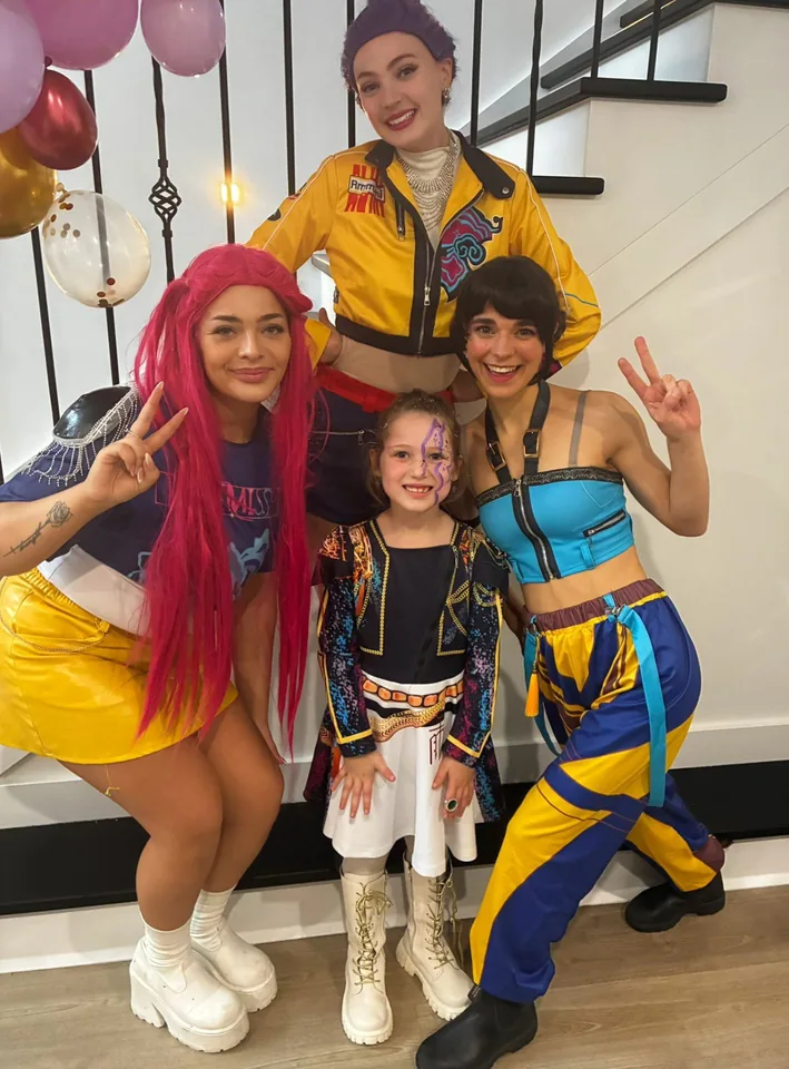 K-Pop Demon Hunters Rumi, Zoey and Mira party entertainers posing with young birthday girl in Huntr/x costume on the stairs at a Melbourne K-Pop Demon Hunters themed birthday party