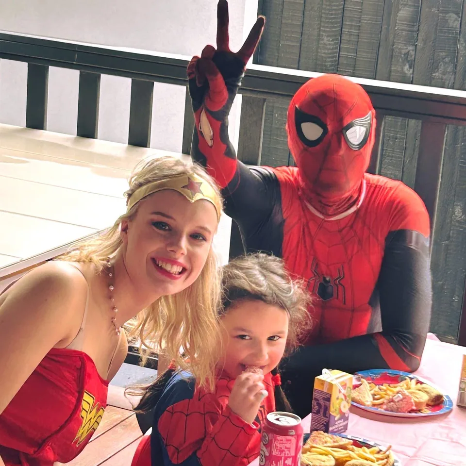 Wonder Woman and Spider-Man party entertainers throwing peace signs with young girl in Spider-Man costume at a Melbourne backyard superhero birthday lunch