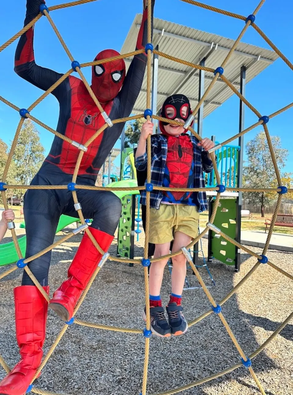 Spider-Man party entertainer climbing a rope dome with young boy in Spider-Man costume and mask at a Melbourne playground birthday party