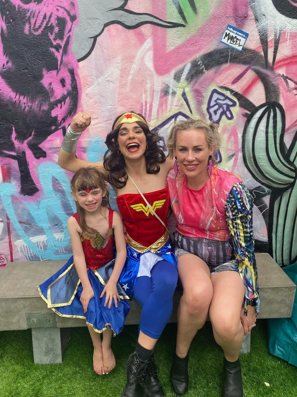 Wonder Woman party entertainer with raised fist posing with young girl in Wonder Woman costume and mum at a Melbourne superhero themed birthday party