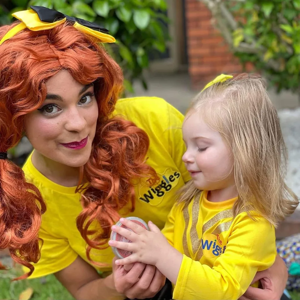 Emma Wiggle character entertainer with red curls and yellow bow cuddling toddler in matching Wiggles yellow top at a Melbourne Wiggles themed birthday party