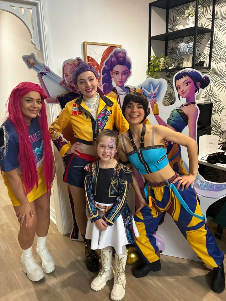 K-Pop Demon Hunters Rumi, Zoey and Mira party entertainers with young girl in matching Huntr/x outfit in front of K-Pop Demon Hunters movie cardboard cutouts at a Melbourne birthday party