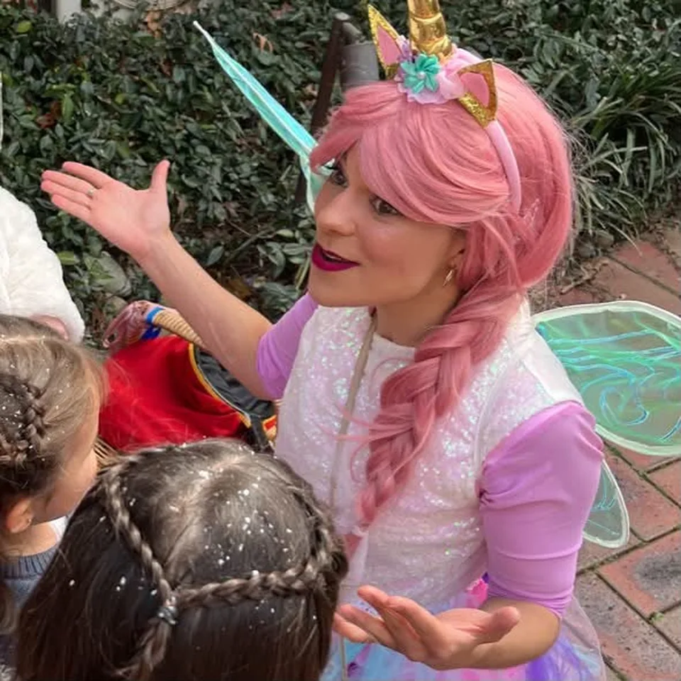 Unicorn fairy party entertainer with long pink braided hair, gold unicorn horn headband and iridescent wings chatting with young girls at a Melbourne unicorn themed birthday party