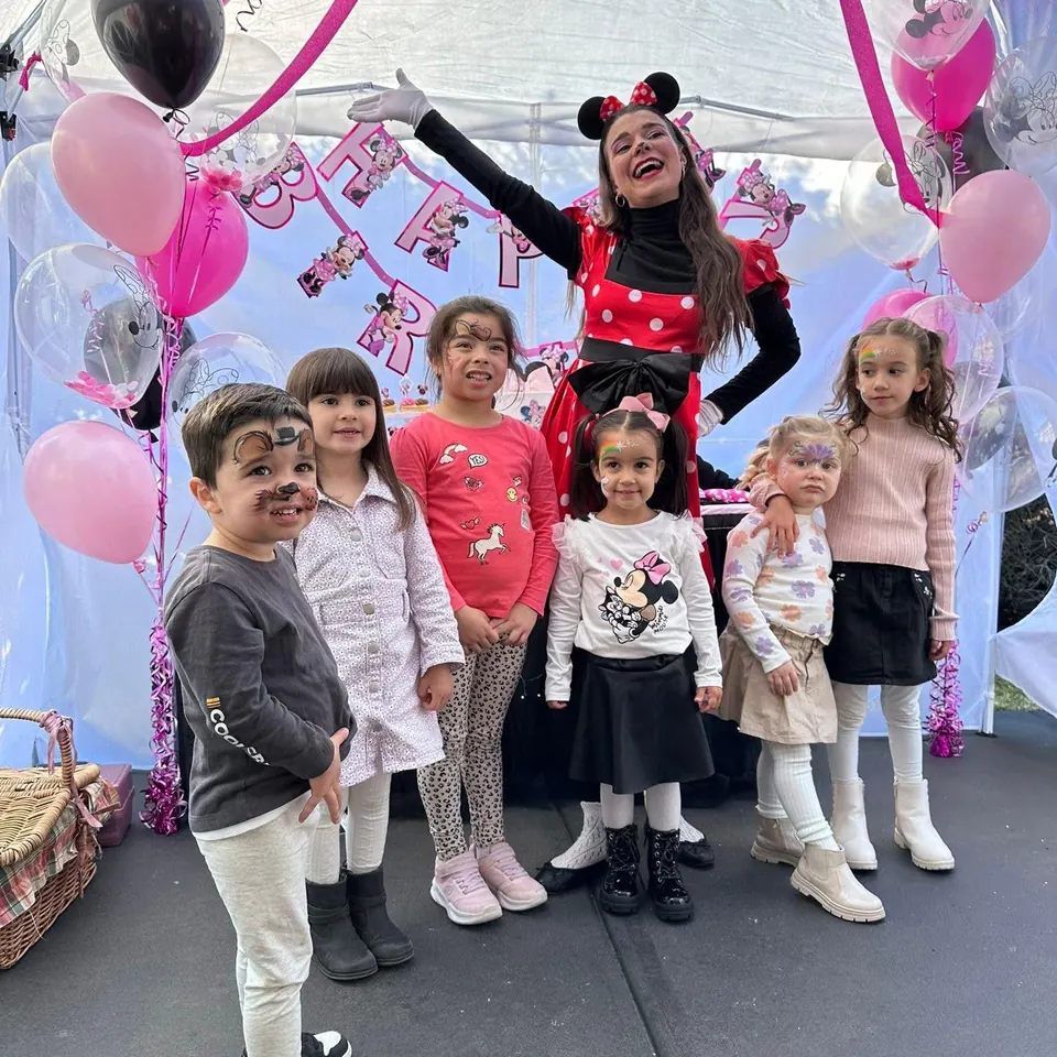 Minnie Mouse party entertainer cheering with group of kids in face paint under a pink Minnie Mouse Happy Birthday marquee at a Melbourne kids party