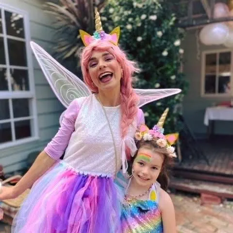 Unicorn fairy party entertainer with pink hair, horn and wings posing with girl in rainbow sequin dress and unicorn headband at a Melbourne backyard birthday party