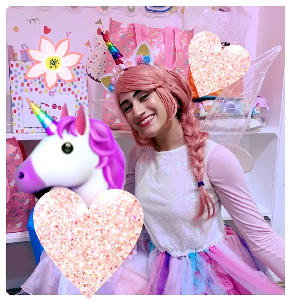 Unicorn fairy party entertainer with pink braided hair, rainbow unicorn horn and shimmering wings smiling beside a unicorn plush at a Melbourne unicorn themed birthday party
