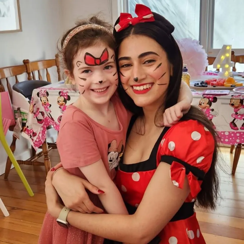 Minnie Mouse party entertainer in red polka dot dress hugging girl with red bow face paint at a Melbourne Minnie Mouse themed birthday party