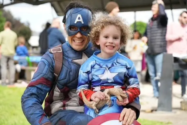 Captain America superhero party entertainer with young boy in Captain America costume holding a bearded dragon at a Melbourne outdoor party