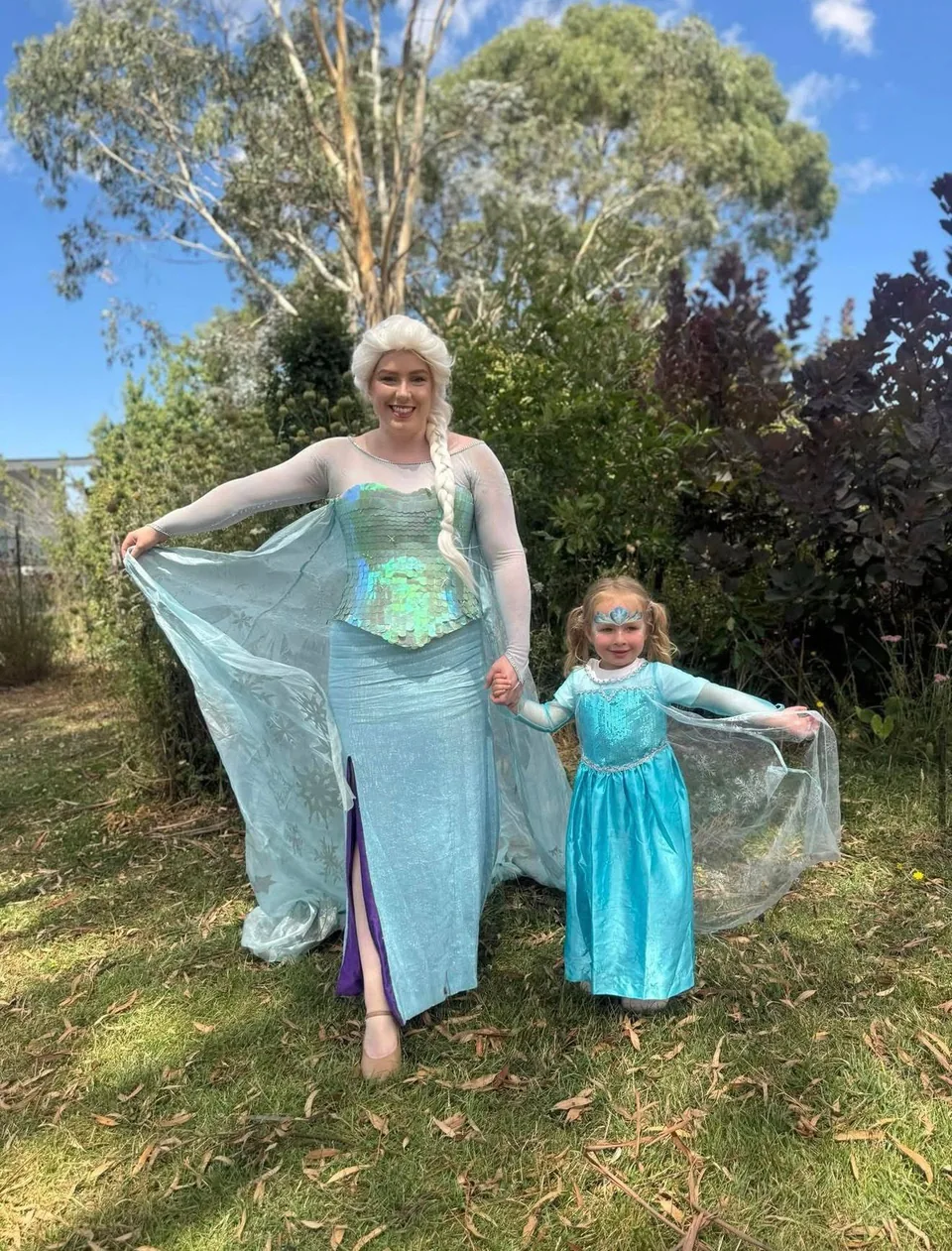 Frozen Elsa party entertainer in sparkling blue gown holding hands with young girl in Elsa dress and tiara in a sunny Melbourne garden princess party