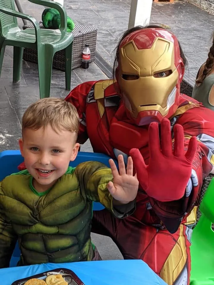 Iron Man party entertainer in red and gold armoured suit waving beside young boy in Hulk muscle costume at a Melbourne outdoor superhero birthday party